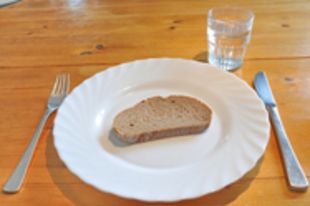 Teller mit einer Scheibe Brot, Besteck daneben und ein Glas Wasser dahinter